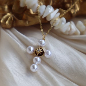 Puede incluir: Un collar de cadena dorada con un colgante de cruz de perlas. La cruz est&aacute; adornada con una peque&ntilde;a estrella brillante en el centro.