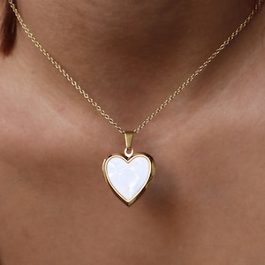 May include: A gold chain necklace with a white heart-shaped locket pendant.
