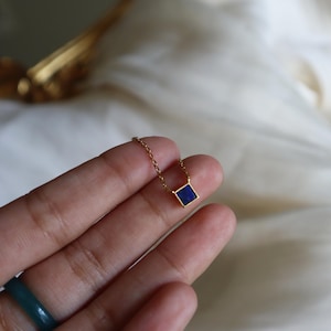 Peut inclure: Un collier en cha&icirc;ne dor&eacute;e avec un petit pendentif carr&eacute; orn&eacute; d'une pierre pr&eacute;cieuse bleu fonc&eacute;.