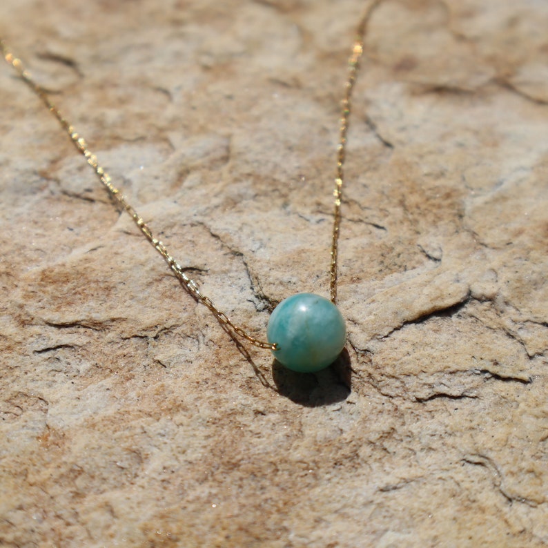 May include: A delicate gold chain necklace with a single, round, light blue gemstone pendant.