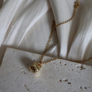 May include: A gold chain necklace with a small, textured, gold cup pendant.