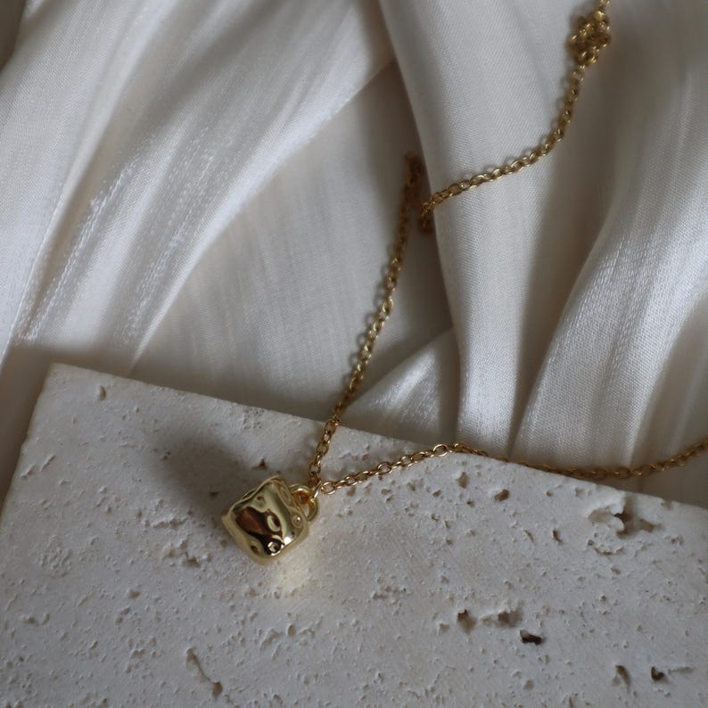 May include: A gold chain necklace with a small, textured, gold cup pendant.