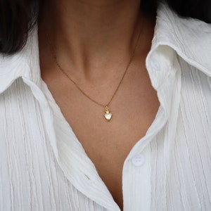 May include: A gold chain necklace with a small white heart pendant. The pendant has a gold crown on top.