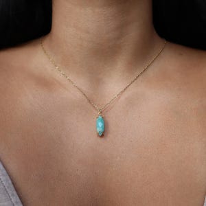K&ouml;nnte beinhalten: Eine zarte goldene Halskette mit einem Anh&auml;nger aus hellblauem, facettiertem Edelstein. Der Anh&auml;nger hat eine l&auml;ngliche ovale Form. Die Halskette wird um den Hals getragen.
