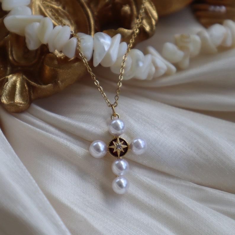 Puede incluir: Un collar de cadena dorada con un colgante de cruz de perlas. La cruz est&aacute; adornada con una peque&ntilde;a piedra brillante en el centro.
