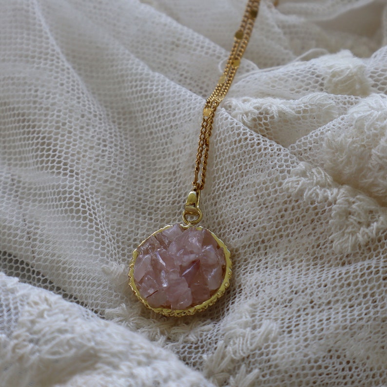 May include: A gold chain necklace with a round pendant featuring a cluster of pink rose quartz crystals.