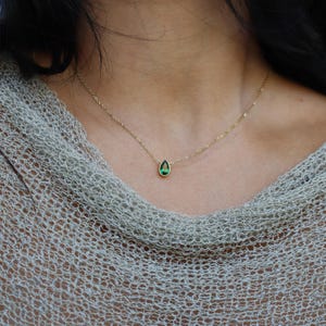 Op de afbeelding: Een delicate gouden ketting met een druppelvormige, smaragdgroene edelsteen hanger. De hanger is gezet in goud en hangt aan een fijne gouden ketting. De ketting wordt getoond tegen een neutrale achtergrond.