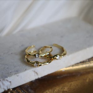 May include: Three gold rings with a textured finish and a single clear stone on each ring.