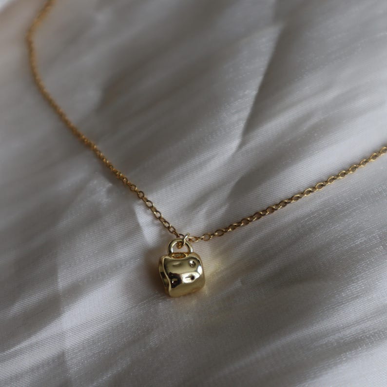 May include: A gold chain necklace with a small, textured, gold pendant shaped like a cylinder.