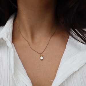 May include: A delicate gold chain necklace with a small, white heart-shaped pendant.