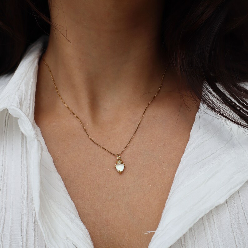 May include: A delicate gold chain necklace with a small, white heart-shaped pendant.