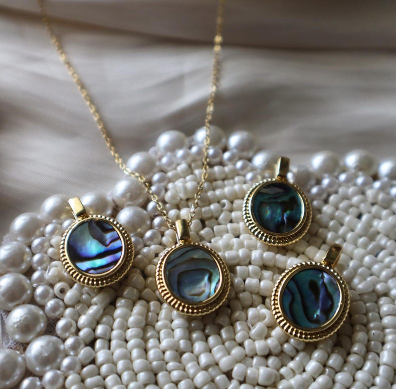 May include: A gold-toned necklace and three matching pendants, each featuring a circular abalone shell inlay with iridescent blue, green, and purple hues. The pendants are framed by a textured, ridged gold-toned metal border with a small bail.