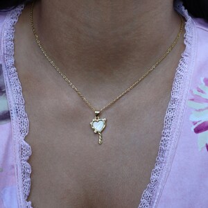 May include: A gold chain necklace with a heart-shaped pendant. The pendant is made of white mother-of-pearl and has a small key design at the bottom.