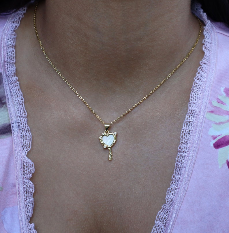 May include: A gold chain necklace with a heart-shaped pendant. The pendant is made of white mother-of-pearl and has a small key design at the bottom.