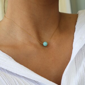 May include: A delicate gold chain necklace with a single round turquoise gemstone pendant.