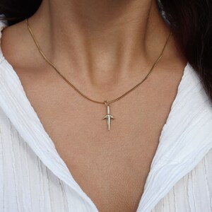 Puede incluir: Un collar de cadena de oro con un peque&ntilde;o colgante de daga.