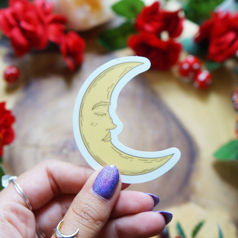 May include: A yellow crescent moon sticker with a closed eye and a smiling mouth. The sticker is on a white background.