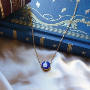 Peut inclure: Un collier en cha&icirc;ne dor&eacute;e avec un pendentif &oelig;il turc bleu et blanc. Le pendentif est rond et a un centre blanc avec un cercle bleu autour.