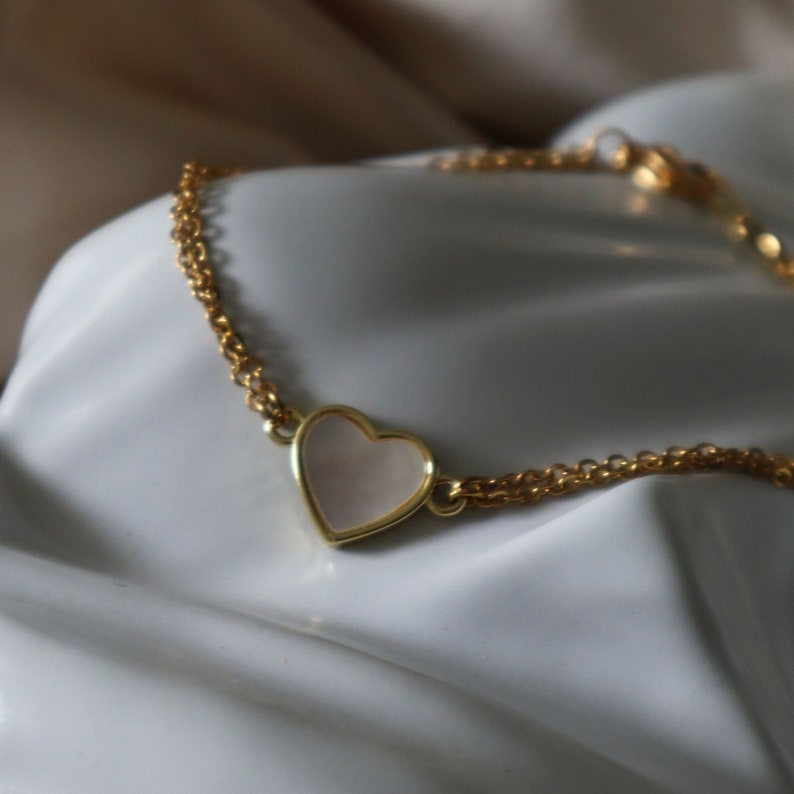 May include: A gold chain bracelet with a white heart-shaped pendant.