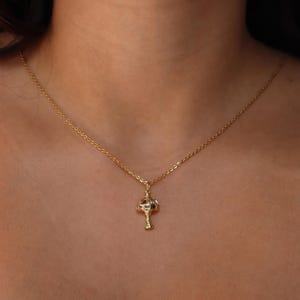 May include: A gold chain necklace with a small, ornate pendant shaped like a lamp with red and white accents.