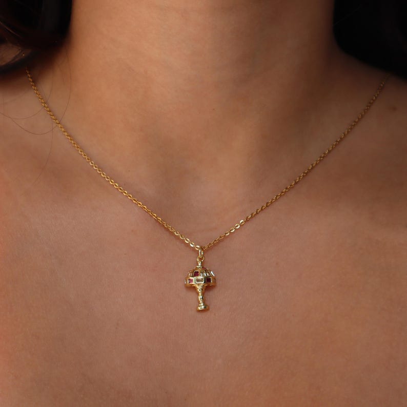 May include: A gold chain necklace with a small, ornate pendant shaped like a lamp with red and white accents.