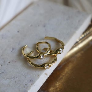 May include: Three gold rings with a textured finish and a single clear stone on each ring.