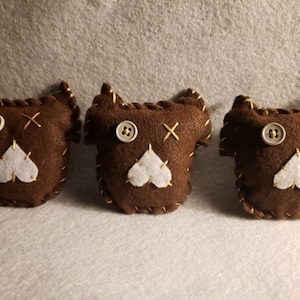 May include: Three brown felt stuffed toys with white felt hearts and button eyes. The toys have gold stitching around the edges.