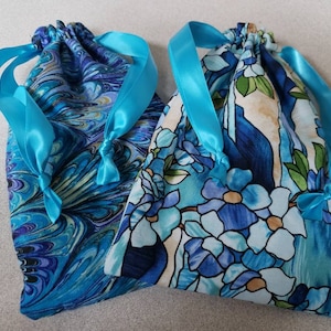 May include: Two blue drawstring bags with turquoise ribbon ties. One bag has a swirling blue and green pattern, the other has a floral pattern with blue and white flowers.
