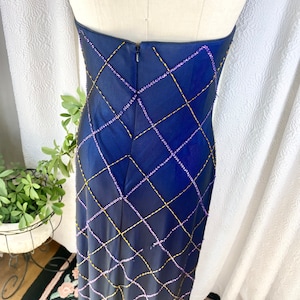 May include: A long, navy blue strapless dress with a diamond pattern created by purple and gold beading. The dress has a zipper in the back.