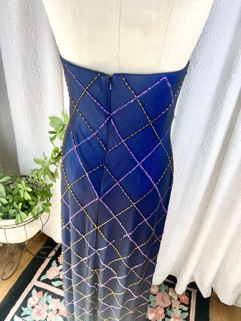 May include: A long, navy blue strapless dress with a diamond pattern created by purple and gold beading. The dress has a zipper in the back.