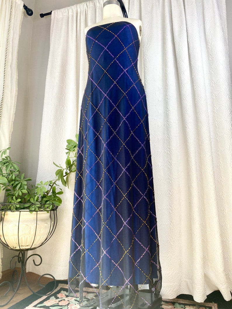 May include: A strapless, floor-length gown in a deep blue color with a diamond-shaped pattern of purple and gold sequins.