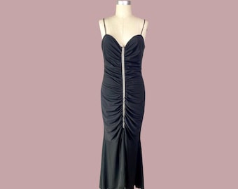 May include: A black evening gown with spaghetti straps and a sweetheart neckline. The dress features a ruched bodice and a vertical line of sparkling embellishments down the center. The skirt flares out slightly at the bottom.