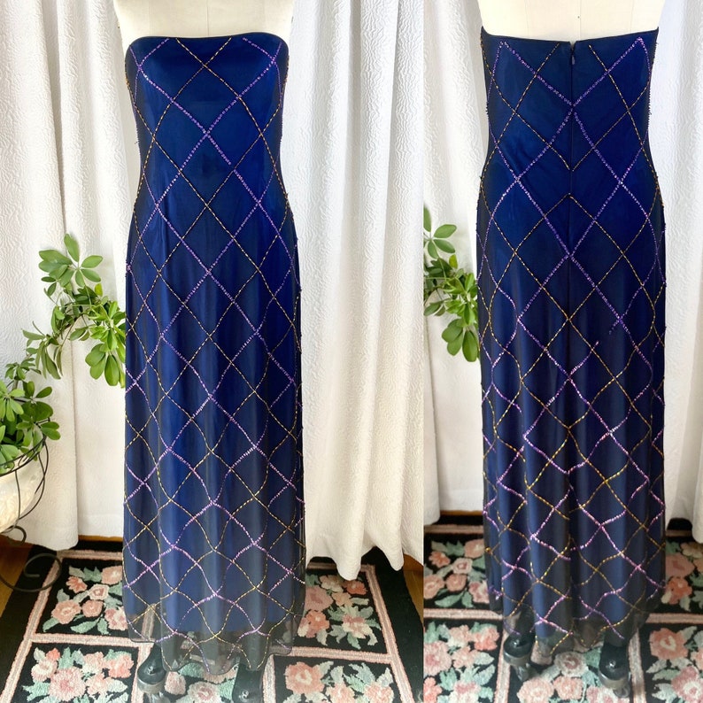 May include: A strapless, floor-length gown in a deep blue color. The gown is adorned with a geometric pattern of sequins in gold, purple, and pink.