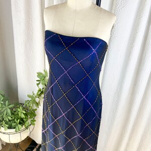 May include: A strapless, floor-length gown in a deep blue color. The gown is adorned with a geometric pattern of gold and purple beads.