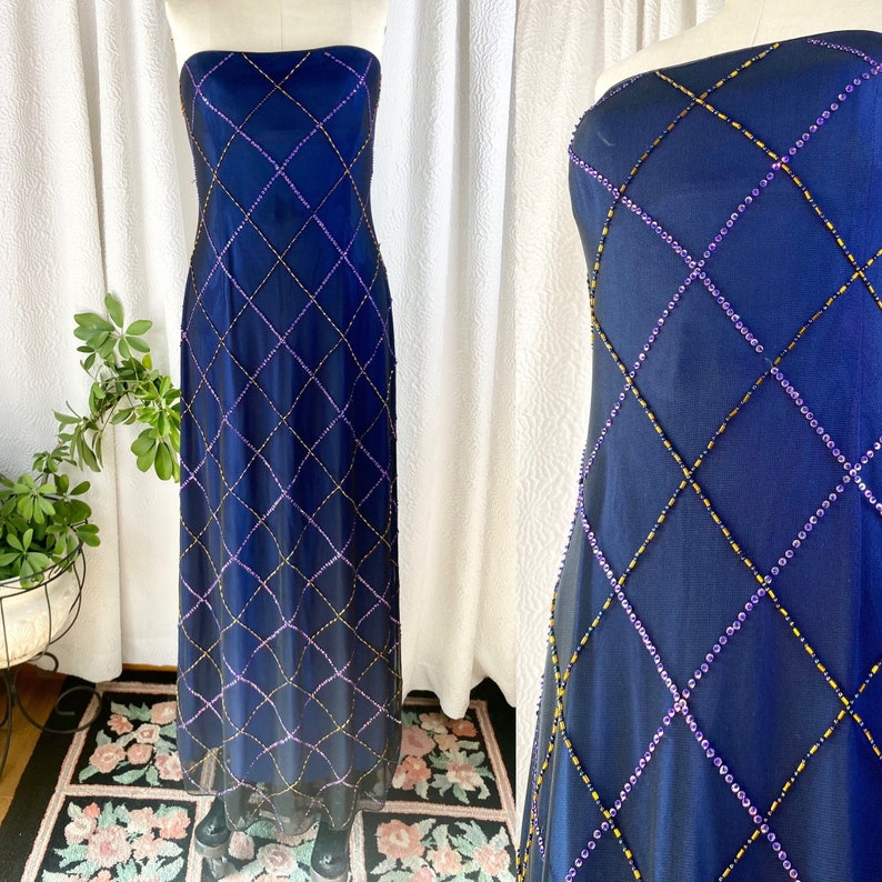 May include: A strapless, floor-length gown in a deep blue color. The gown is adorned with a diamond-shaped pattern of purple and gold beads.