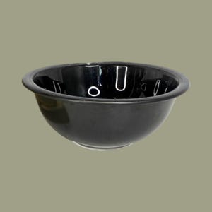 May include: A glossy black bowl with a smooth, rounded interior and a wide, flat rim. The surface of the bowl reflects light, creating bright white highlights along the inner curve and the top edge, emphasizing its deep, dark color and shape.
