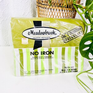 以下が含まれることがあります： Meadowbrookの包装されたフラットシーツ。シーツは緑と白のストライプで、「No Iron」と書かれています。パッケージには、シーツは137 x 190 cmのマットレス用で、綿50％、ポリエステル50％でできていると記載されています。