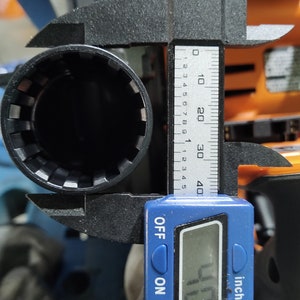Puede incluir: Una herramienta de llave de vaso negra se mide con un calibrador digital. La medida es de 10,2 mm. La herramienta tiene una abertura circular con dientes internos. El calibrador es azul y muestra medidas en pulgadas y mil&iacute;metros.