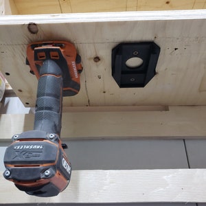 May include: A black and orange cordless drill with a brushless motor is mounted on a wooden shelf. The drill is hanging upside down with the drill bit facing up. The drill is labeled "DEWALT" and "BRUSHLESS".
