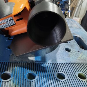 Puede incluir: Una herramienta el&eacute;ctrica naranja y negra con un accesorio de boquilla negro. La herramienta est&aacute; colocada sobre un banco de trabajo azul con agujeros circulares. La imagen est&aacute; tomada desde una perspectiva cercana, destacando el dise&ntilde;o y las caracter&iacute;sticas de la herramienta.