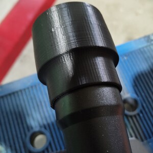 Puede incluir: Un adaptador de pl&aacute;stico negro con un dise&ntilde;o escalonado, probablemente para una herramienta o m&aacute;quina. El adaptador tiene forma cil&iacute;ndrica con una secci&oacute;n superior m&aacute;s ancha y una base m&aacute;s estrecha. La superficie muestra l&iacute;neas de capa visibles de la impresi&oacute;n 3D.