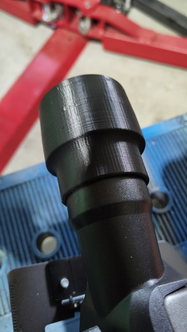 Puede incluir: Un adaptador de pl&aacute;stico negro con un dise&ntilde;o escalonado, probablemente para una herramienta o m&aacute;quina. El adaptador tiene forma cil&iacute;ndrica con una secci&oacute;n superior m&aacute;s ancha y una base m&aacute;s estrecha. La superficie muestra l&iacute;neas de capa visibles de la impresi&oacute;n 3D.