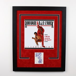 May include: A framed album cover featuring a photo of two men in red and yellow clothing. The album cover is titled "Rob Base & D.J.E-Z Rock It Takes Two" and features the text "featuring It Takes Two Joy And Pain Don't Sleep On It and more!" The album cover is signed by Rob Base and D.J.E-Z Rock.