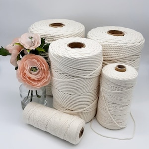 May include: Four spools of natural cotton rope in various sizes. The rope is thick and has a natural, off-white colour. The spools are arranged in a pyramid shape on a white surface.