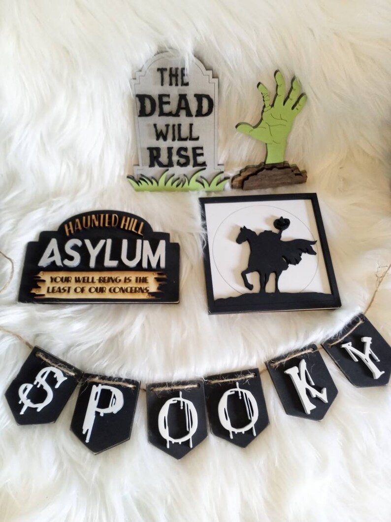 Pode incluir: Um conjunto de decora&ccedil;&otilde;es de Halloween que inclui uma placa preta e branca que diz "Haunted Hill Asylum Your Well-Being Is The Least Of Our Concerns", uma placa preta e branca com uma silhueta de um cavaleiro a cavalo, uma l&aacute;pide branca com texto preto que diz "The Dead Will Rise", uma m&atilde;o de zumbi verde e uma faixa preta e branca que diz "Spooky".