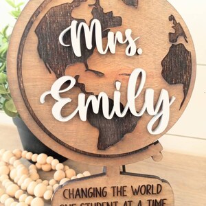 K&ouml;nnte beinhalten: Holzkugel mit dem Text "Mrs. Emily" und dem Spruch "Die Welt ver&auml;ndern, ein Sch&uuml;ler nach dem anderen".