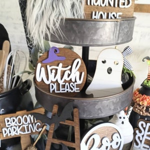 May include: A three-tiered metal stand decorated with Halloween-themed items. The top tier features a wooden sign that says "Haunted House", the middle tier has a wooden sign that says "Witch Please", and the bottom tier has a wooden sign that says "Broom Parking".