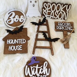 May include: A set of seven wooden Halloween signs with white lettering. The signs include "Boo", "Spooky Season", "Haunted House", "Broom Parking", "Witch Please", and two bats.