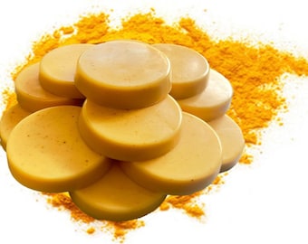 May include: A stack of smooth, round, mustard-yellow soap bars with a flat top and bottom, arranged in a circular cluster. The soap bars are resting on a bed of loose, vibrant yellow powder that surrounds the base of the stacked items.