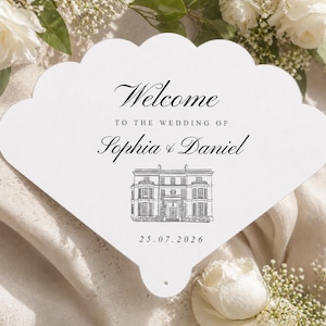 Peut inclure: Éventail de mariage blanc à bord festonné. Il porte l'inscription "Welcome to the Wedding of Sophia & Daniel" en écriture noire. Une illustration détaillée d'un bâtiment et la date 25.07.2026 sont également présentes.